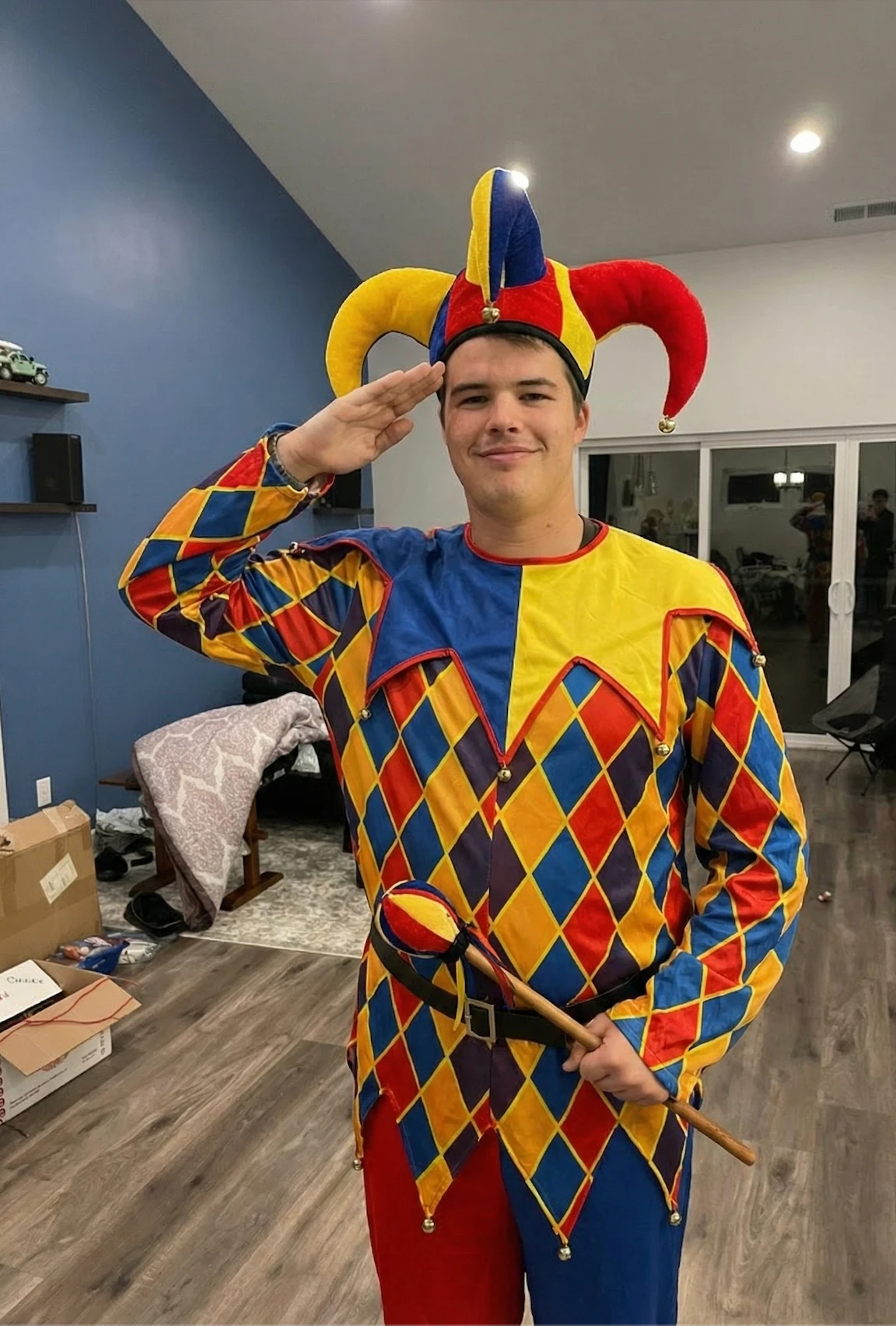 Braidon in a red, yellow and blue harlequin jester costume, saluting